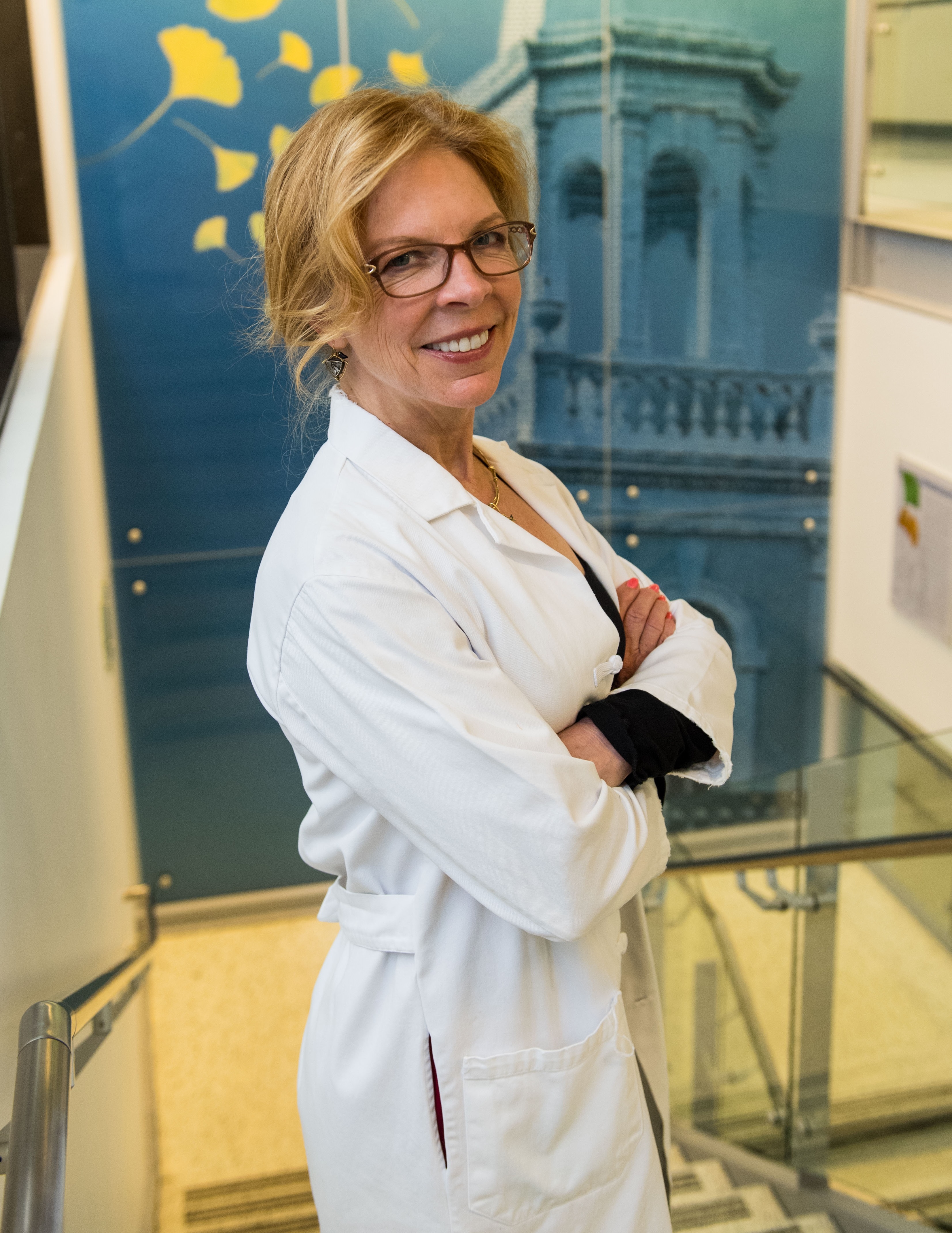 Photo of Kathryn Sandberg, PhD standing in a bright stairway wearing a white lab coat
