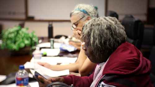 Two members of the GHUCCTS Participant Advisory Board reading a packet at a conference table