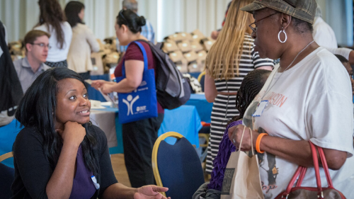 Two women talking to each other across an information table at a resource fair